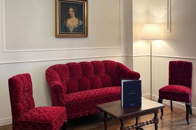 Salon avec canapé et chaises en velours rouge, table basse en bois, lampe sur pied et tableau au mur.