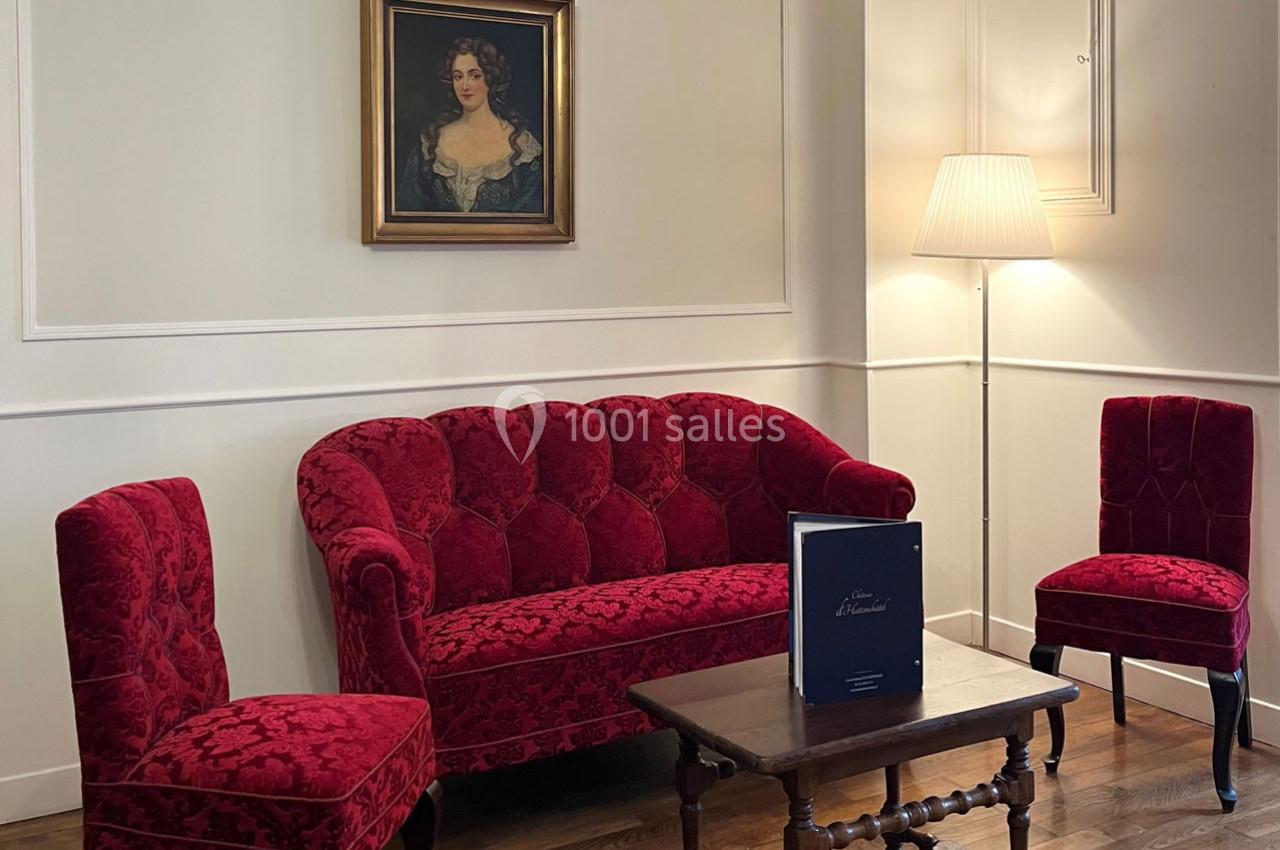 Salon avec canapé et chaises en velours rouge, table basse en bois, lampe sur pied et tableau au mur.