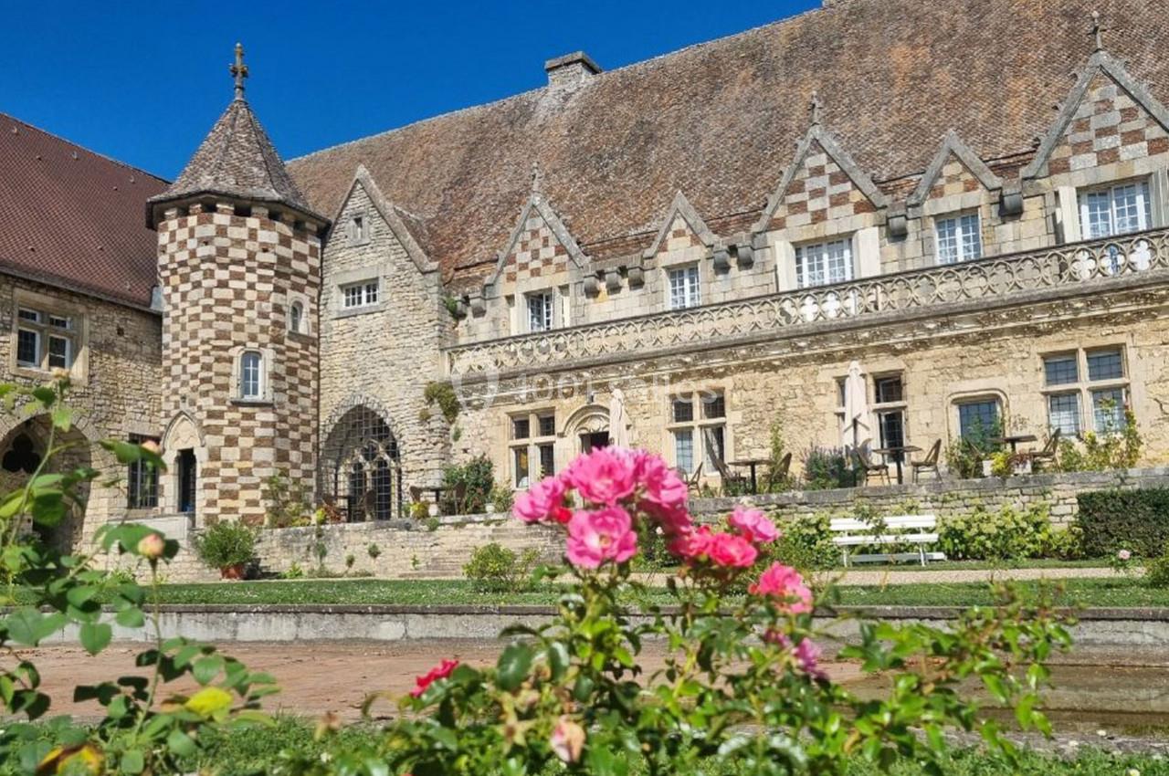 Façade d'un bâtiment historique en pierre avec toit en tuiles, devant un jardin fleuri de roses roses.