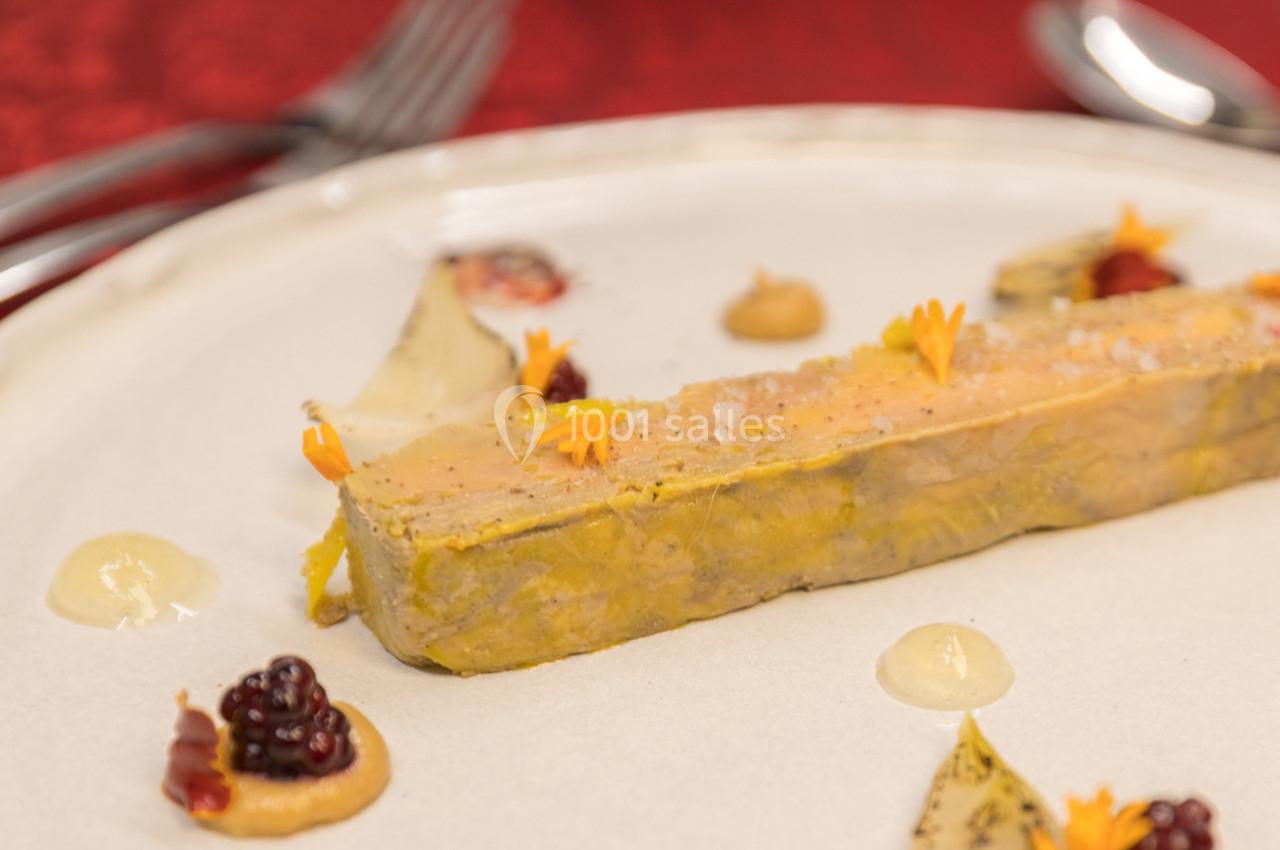 Tranche de foie gras garnie de fleurs comestibles, accompagnée de purées et de fruits sur une assiette blanche.