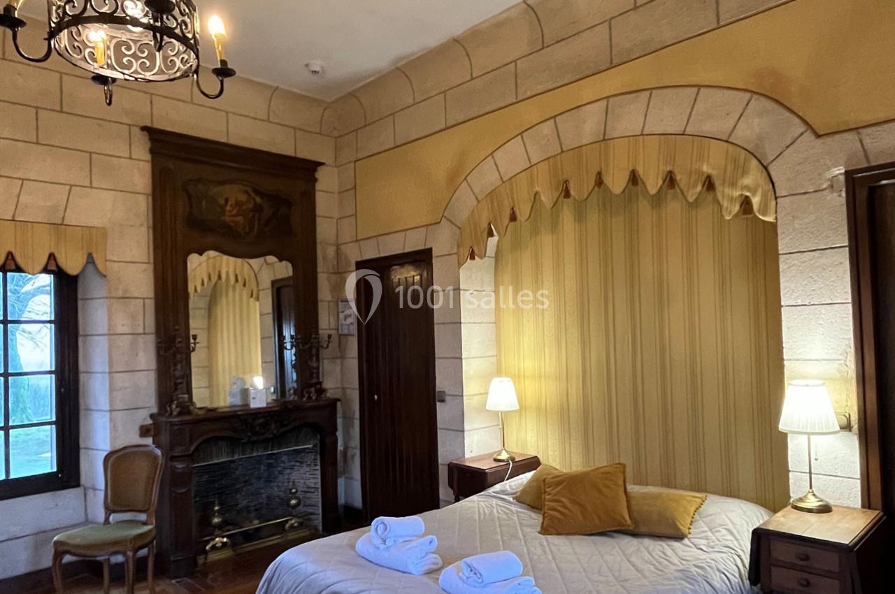 Chambre avec murs en pierre, lit double, cheminée ancienne, miroir, et éclairage doux par des lampes de chevet.