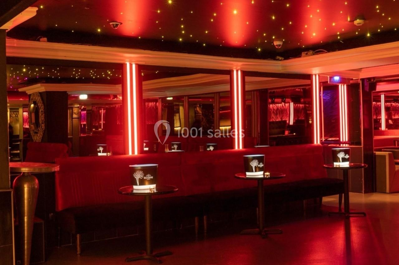 Salle de bar ou club avec éclairage rouge, canapés en velours, tables basses et plafond étoilé lumineux.