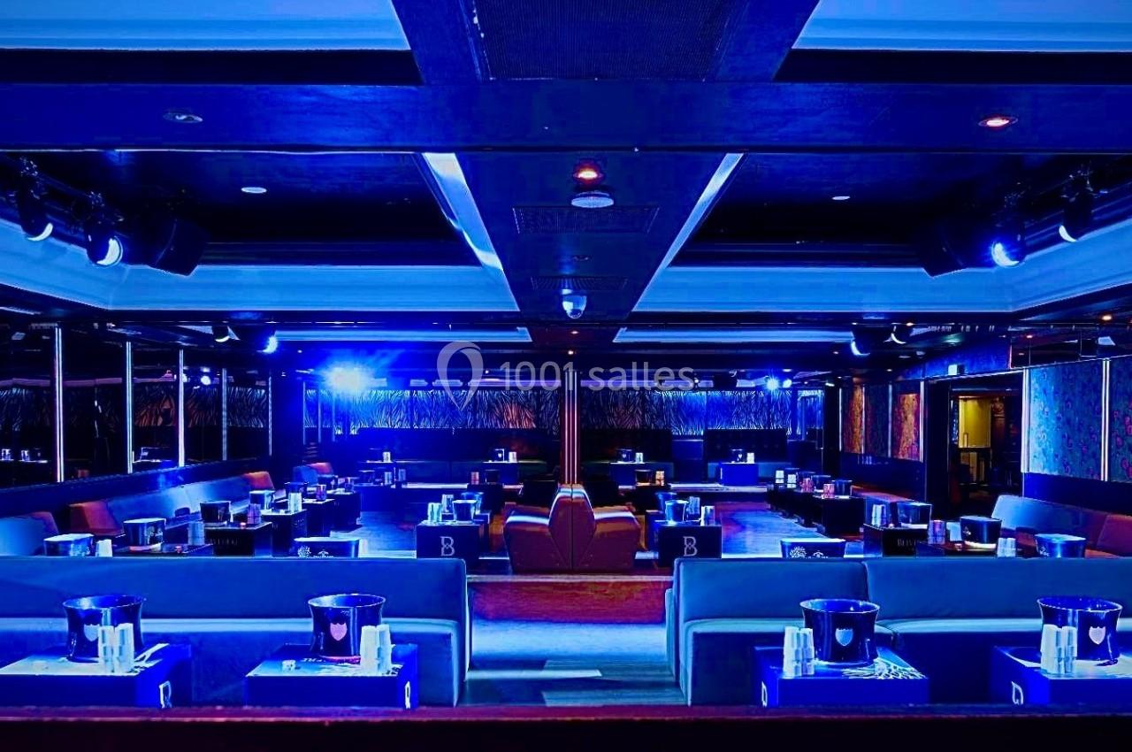 Salle de réception avec éclairage bleu, tables dressées et banquettes alignées dans un espace moderne et élégant.