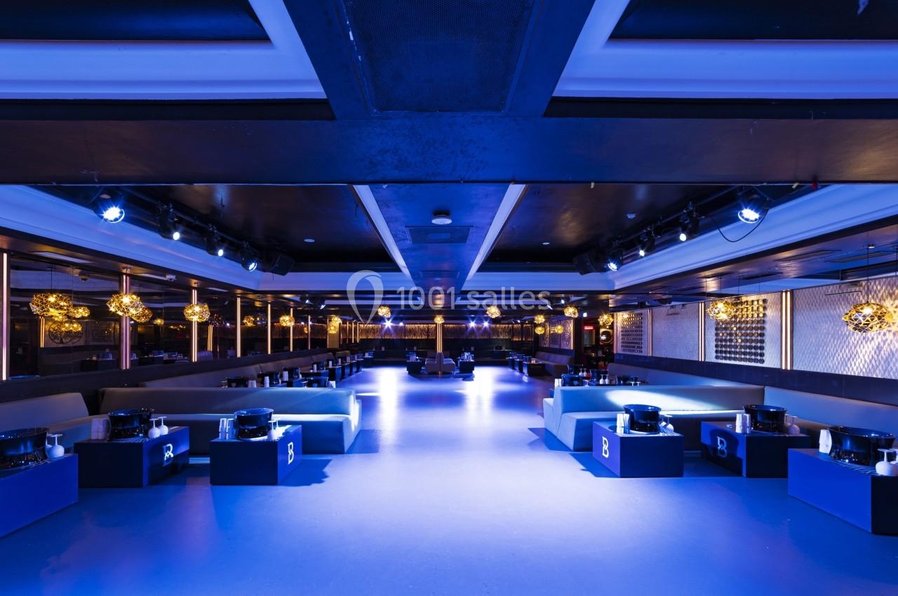 Salle de réception moderne avec éclairage bleu, banquettes, tables basses et décorations lumineuses suspendues.