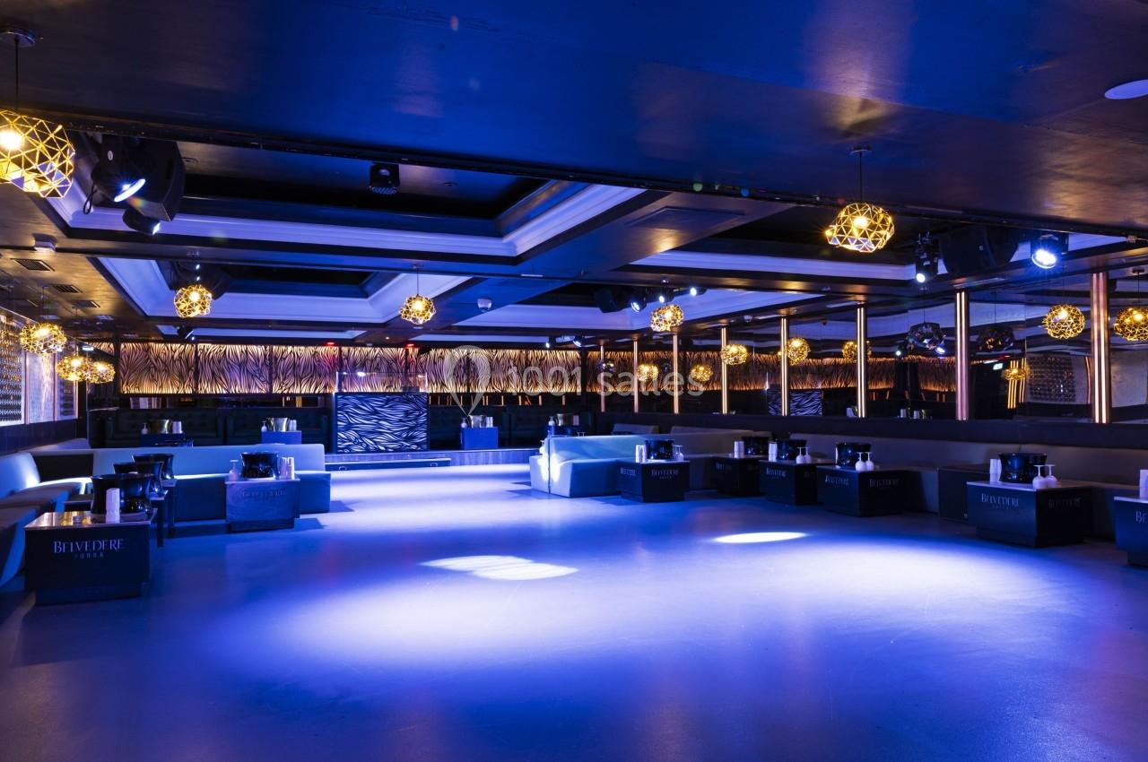 Salle de réception moderne avec éclairage bleu, canapés blancs et décorations lumineuses suspendues.