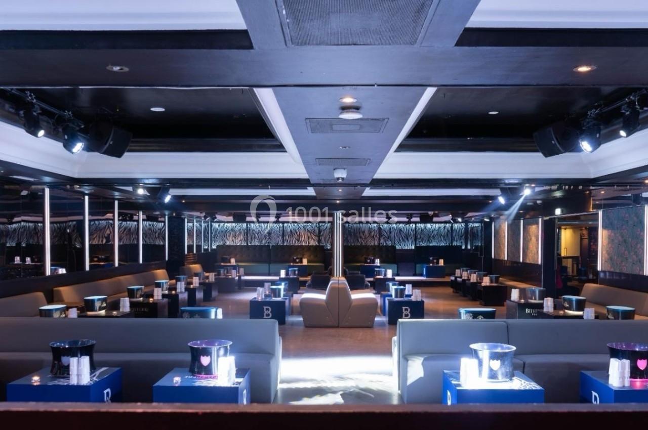 Salle de réception moderne avec banquettes grises, tables bleues et éclairage tamisé.