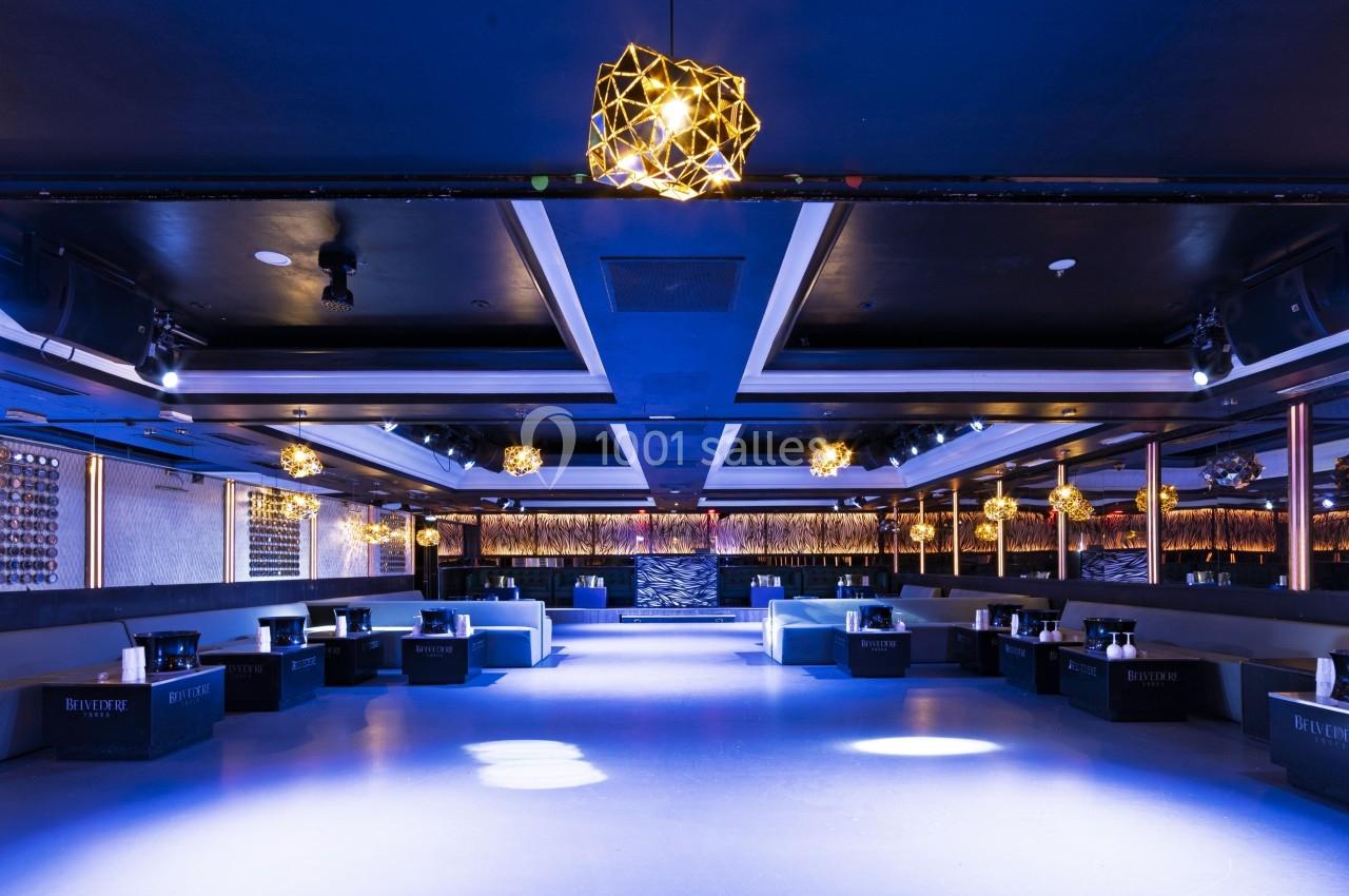 Salle de réception moderne et spacieuse avec éclairage tamisé, banquettes et lustres géométriques suspendus.