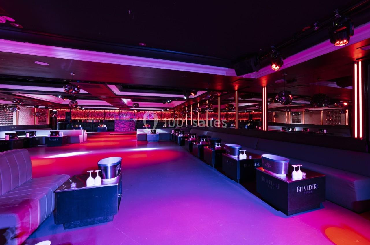 Salle de club vide avec éclairage coloré, banquettes, tables basses et murs ornés de miroirs.