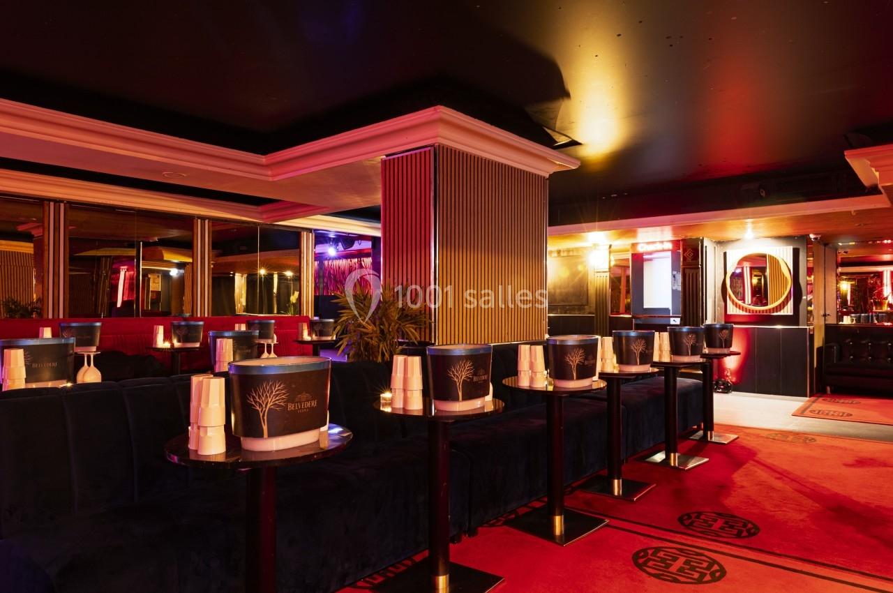 Salle de réception élégante avec banquettes rouges, tables basses noires et éclairage tamisé dans une ambiance nocturne.