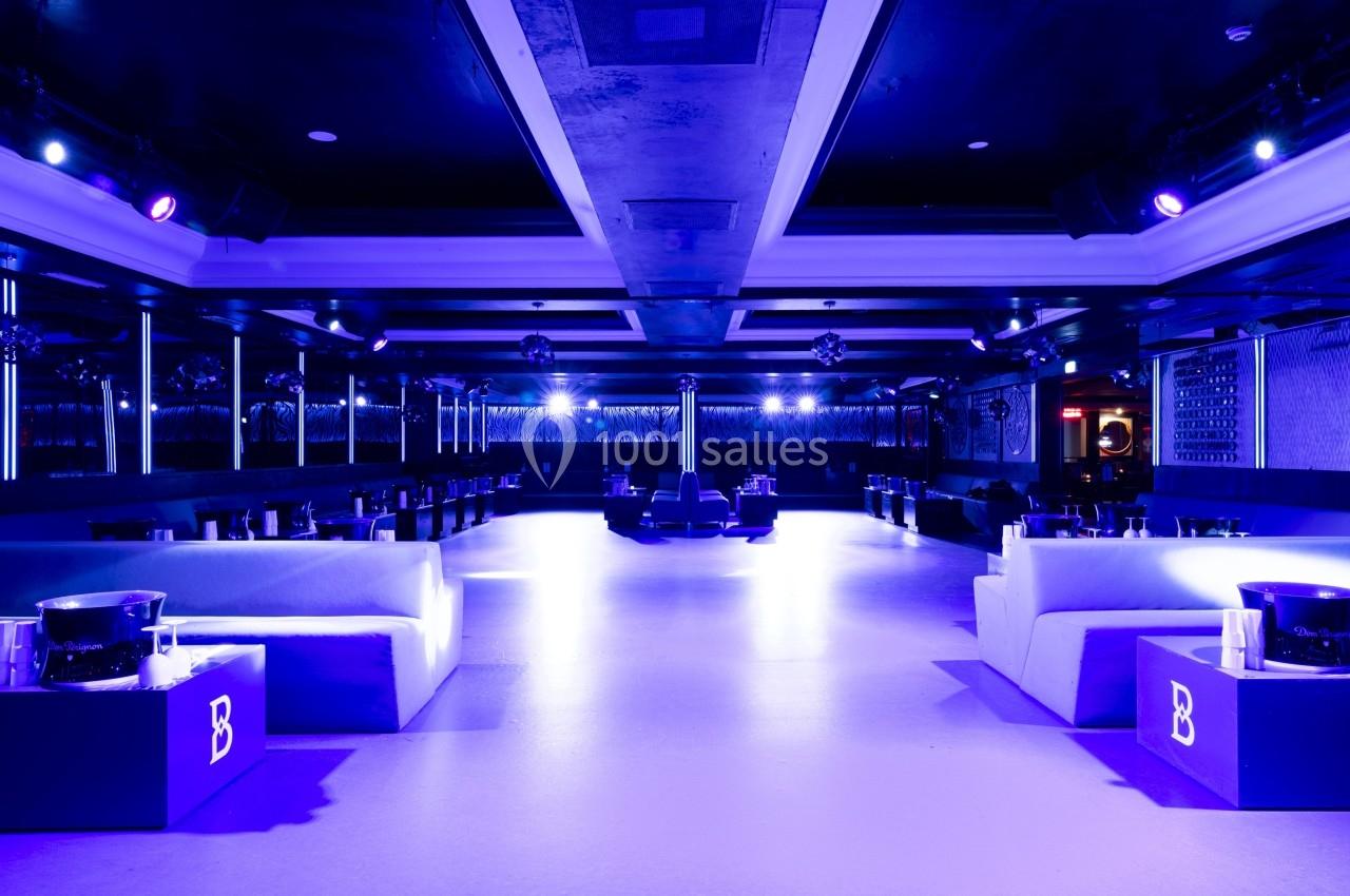 Salle de réception moderne avec éclairage violet, canapés blancs et tables basses disposées symétriquement.