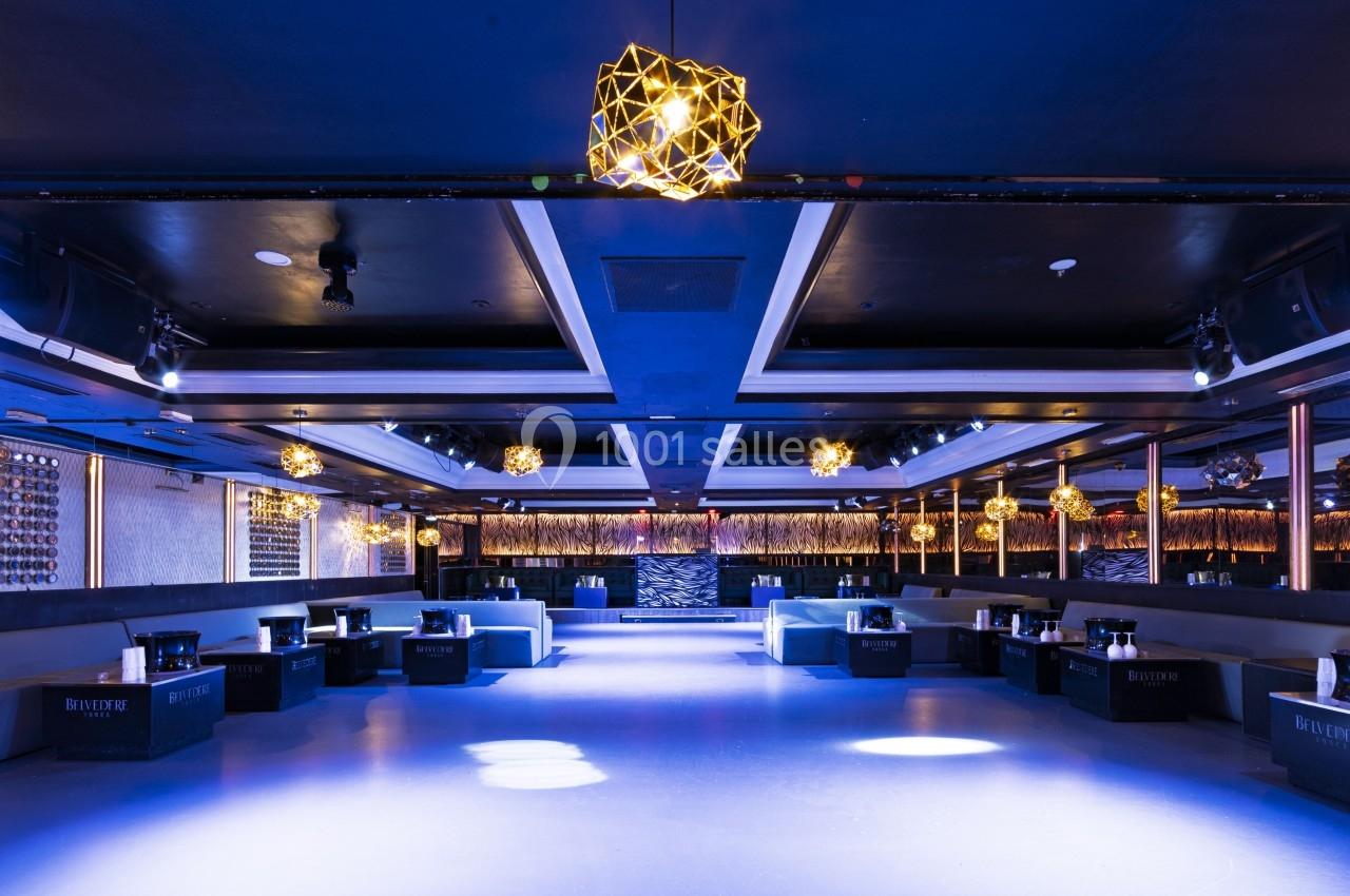 Salle de réception moderne avec éclairage tamisé, canapés alignés et décorations lumineuses suspendues.