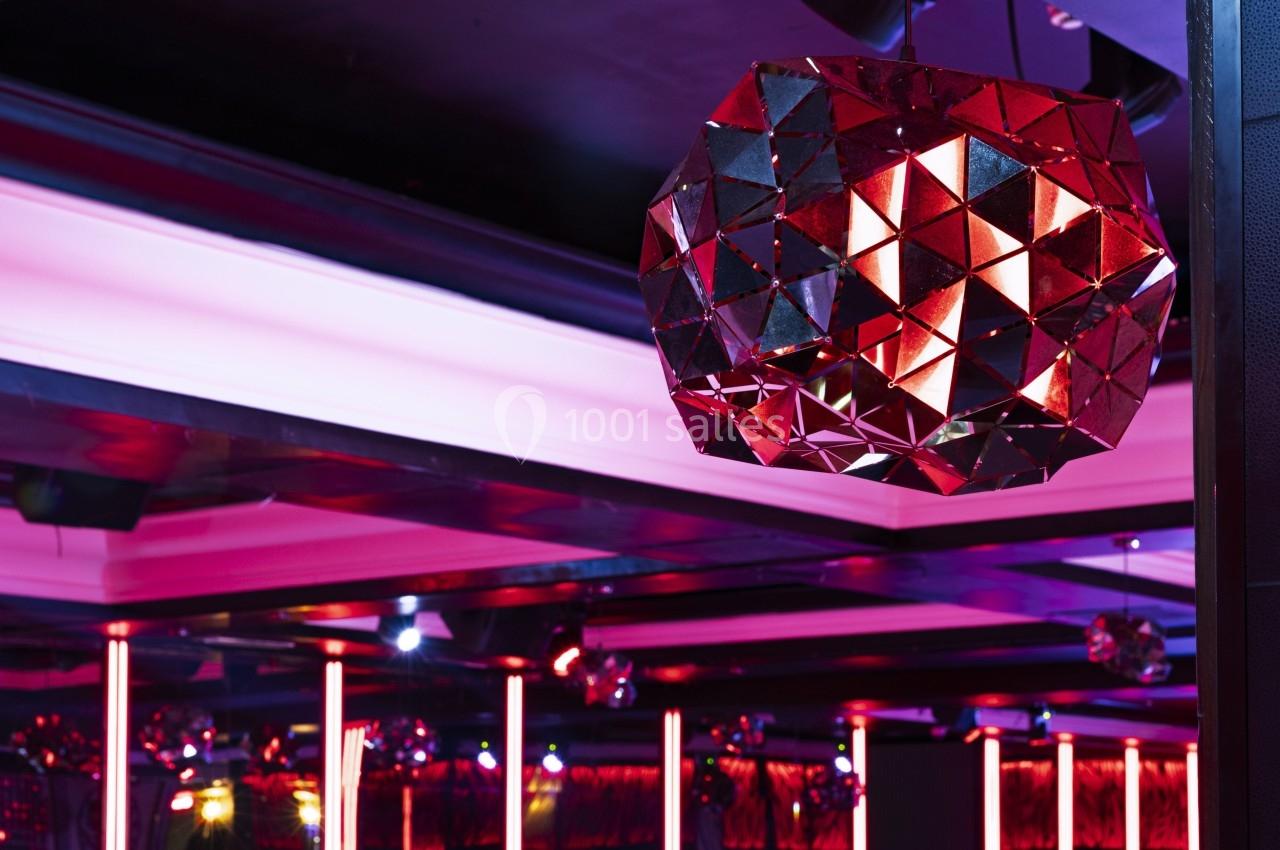 Lustre géométrique rouge suspendu dans un intérieur moderne avec éclairage néon et plafond sombre.