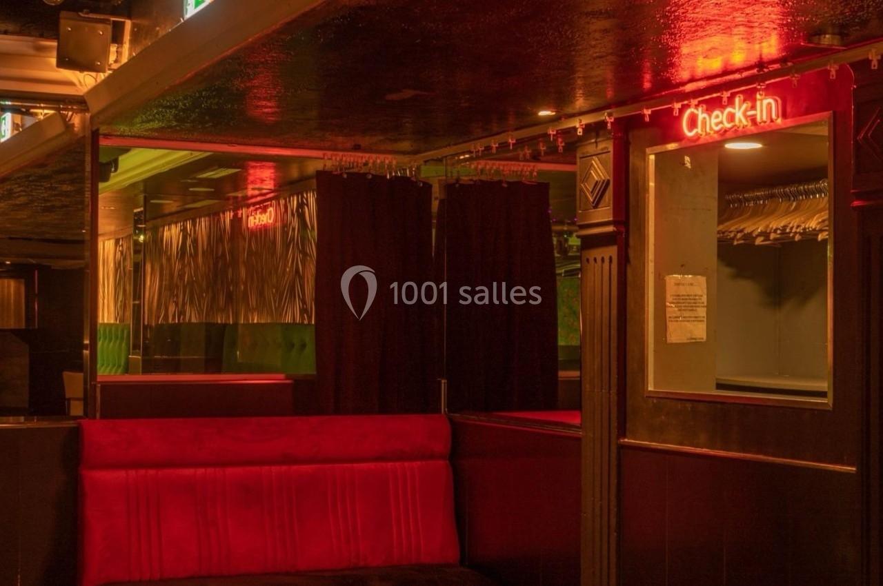 Espace intérieur sombre avec banquette rouge, rideaux noirs et enseigne lumineuse ’Check-in’ au mur.