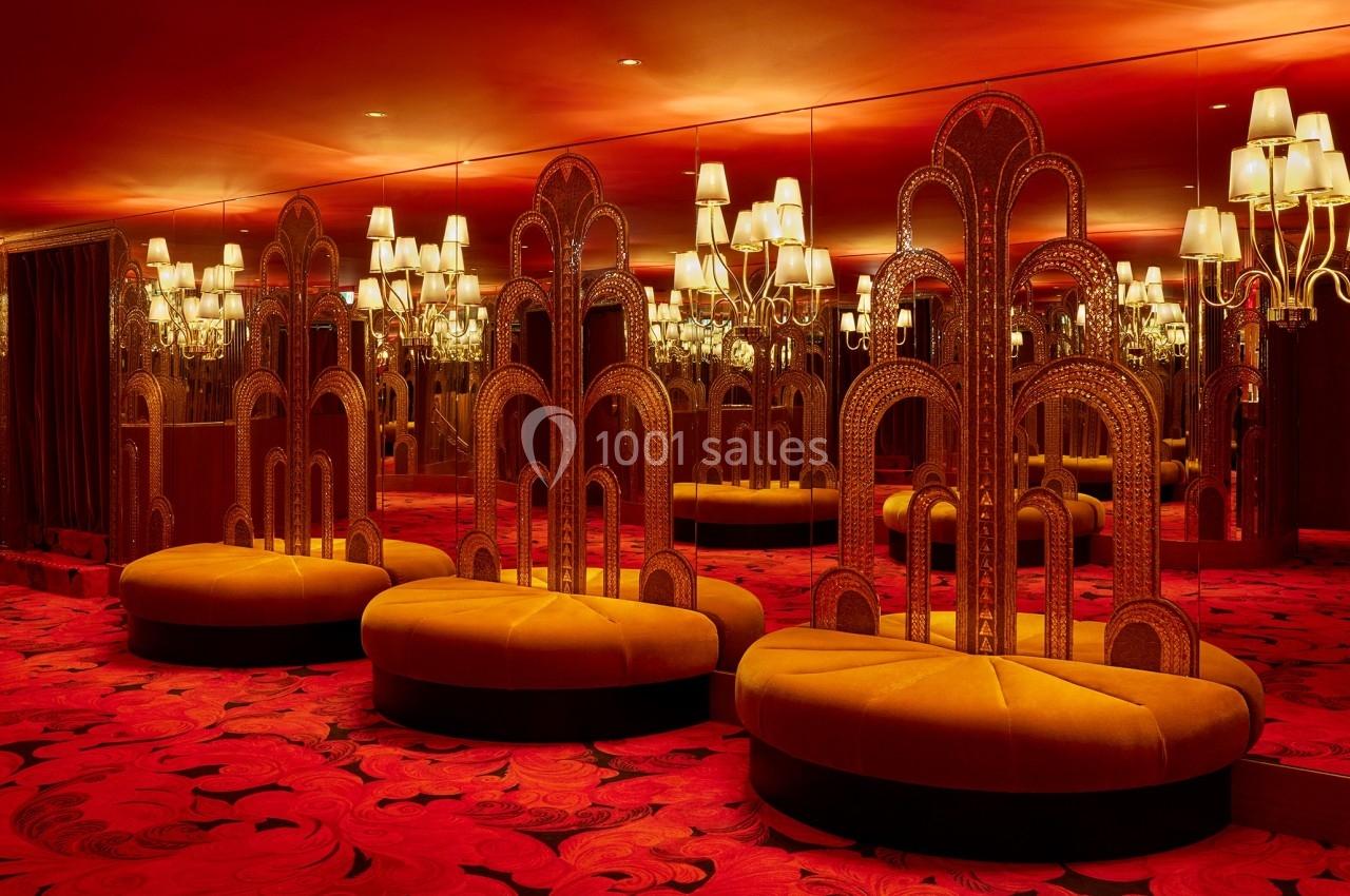 Banquettes jaunes et miroirs entourés de lampes dans une pièce au décor rouge avec motifs au sol.