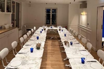 Façade d'un bâtiment en pierre avec terrasse vitrée et bar extérieur bleu, entouré de verdure.