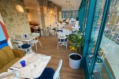 Façade d'un bâtiment en pierre avec terrasse vitrée et bar extérieur bleu, entouré de verdure.