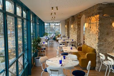 Façade d'un bâtiment en pierre avec terrasse vitrée et bar extérieur bleu, entouré de verdure.