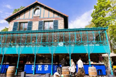 Façade d'un bâtiment en pierre avec terrasse vitrée et bar extérieur bleu, entouré de verdure.