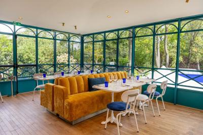 Façade d'un bâtiment en pierre avec terrasse vitrée et bar extérieur bleu, entouré de verdure.