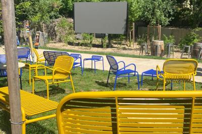 Façade d'un bâtiment en pierre avec terrasse vitrée et bar extérieur bleu, entouré de verdure.