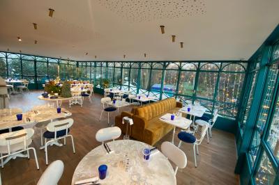 Salle à manger lumineuse avec deux longues tables en marbre blanc, dressées avec des verres bleus et des couverts.
