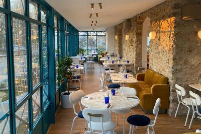 Salle à manger lumineuse avec deux longues tables en marbre blanc, dressées avec des verres bleus et des couverts.