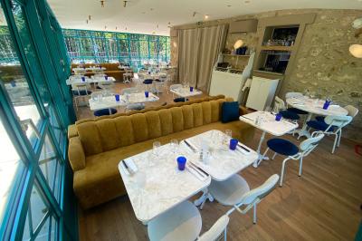 Salle à manger lumineuse avec deux longues tables en marbre blanc, dressées avec des verres bleus et des couverts.