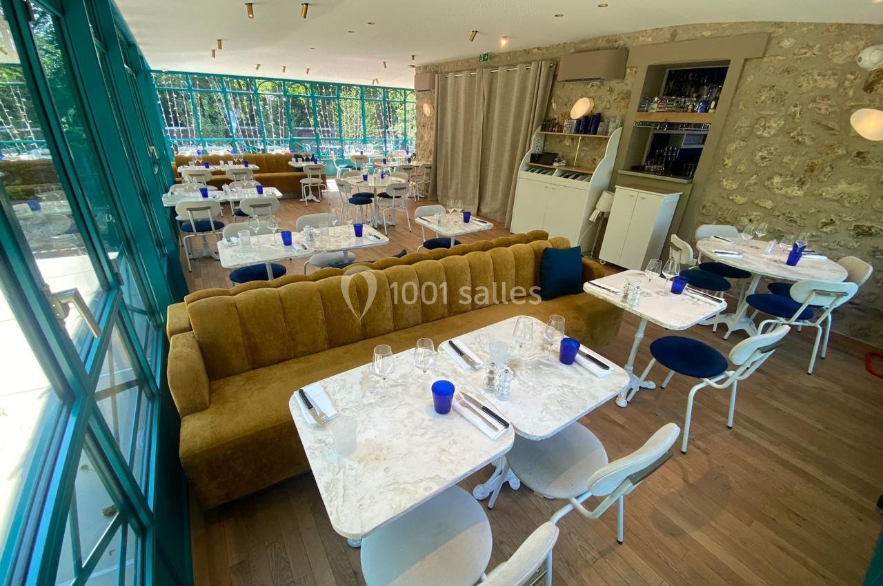 Salle de restaurant lumineuse avec grandes baies vitrées, tables en marbre blanc et banquettes moutarde.