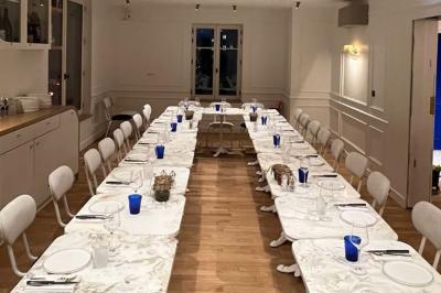 Salle à manger lumineuse avec deux longues tables en marbre blanc, dressées avec des verres bleus et des couverts.