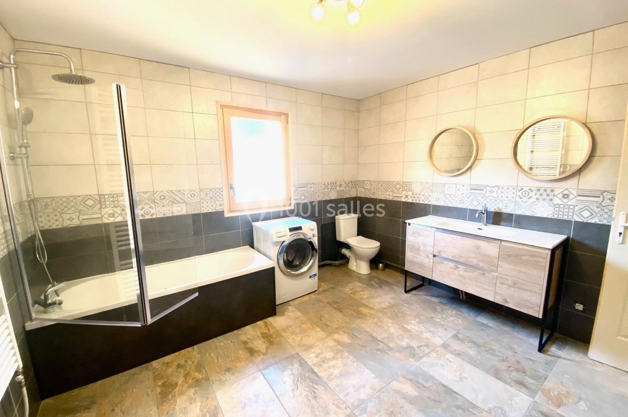 Salle de bain lumineuse avec baignoire, douche, lave-linge, toilettes, meuble vasque double et carrelage beige et gris.