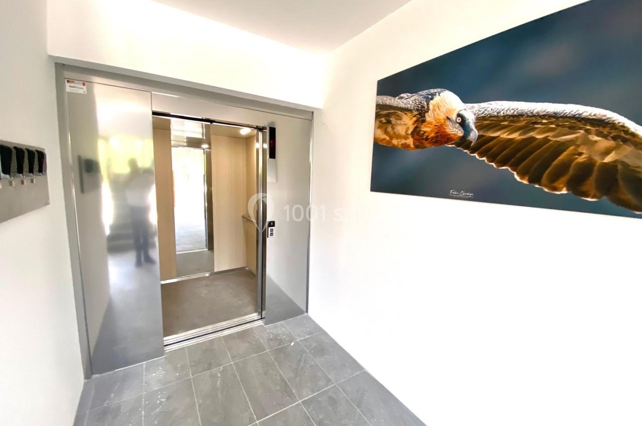 Ascenseur moderne ouvert dans un hall lumineux avec un tableau représentant un oiseau en vol sur le mur.