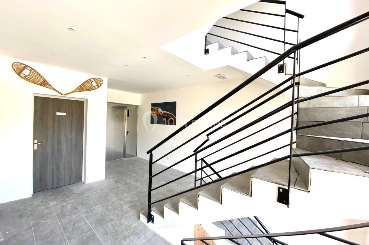 Escalier moderne en métal dans un hall lumineux avec carrelage gris, porte en bois et décoration murale.