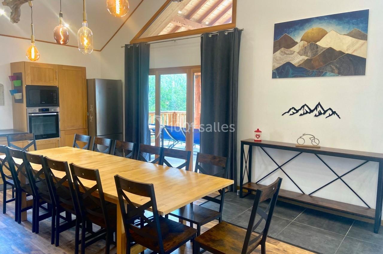 Salle à manger lumineuse avec une grande table en bois, des chaises assorties et une vue sur une terrasse extérieure.