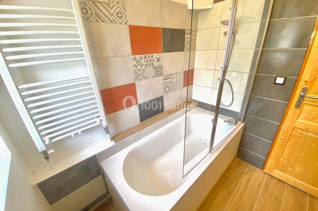 Salle de bain avec baignoire, paroi vitrée, carrelage coloré et motifs, radiateur sèche-serviettes et sol en bois.