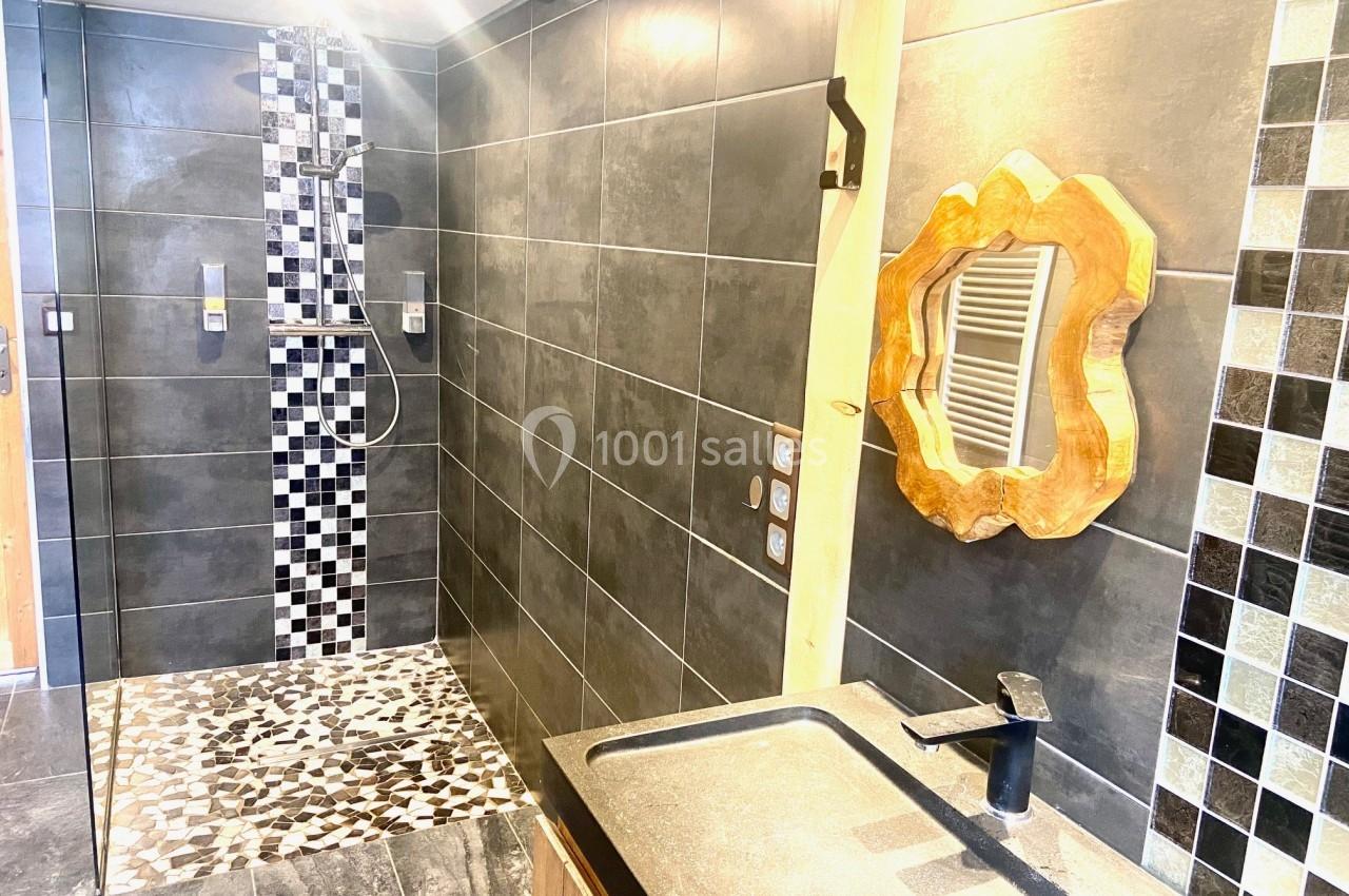 Salle de bain moderne avec douche à l'italienne, carrelage noir et blanc, miroir en bois sculpté et lavabo noir.