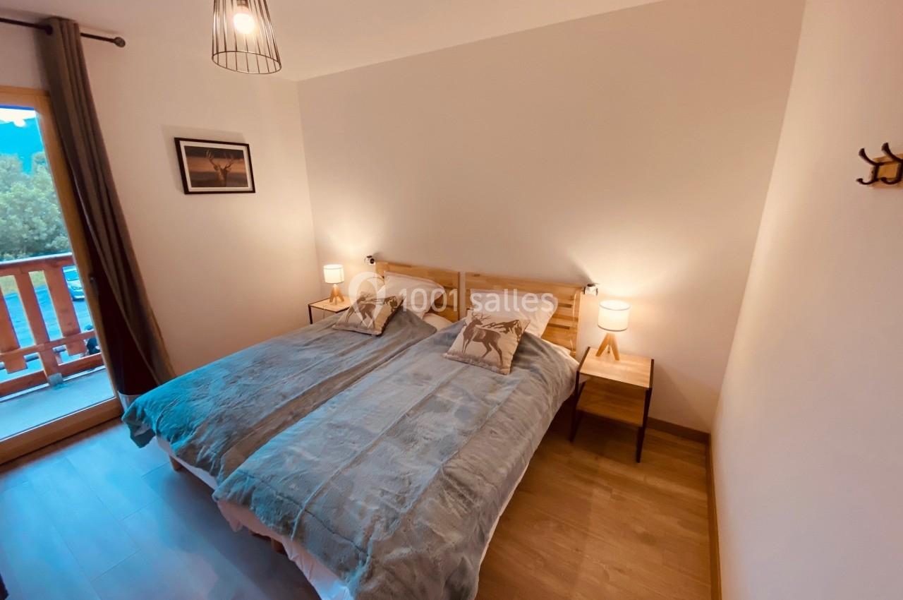 Chambre avec deux lits simples, tablettes de chevet, lampes, parquet et balcon donnant sur un paysage extérieur.