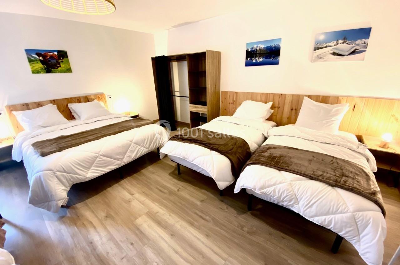 Chambre lumineuse avec deux lits simples et un lit double, parquet au sol, décorations murales et éclairage chaleureux.