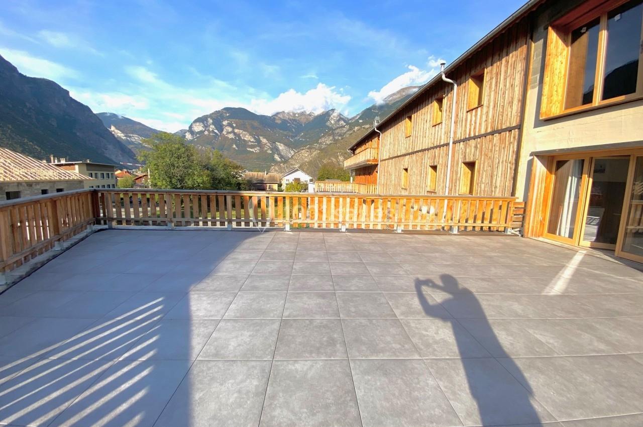 Terrasse spacieuse en carrelage gris avec vue sur des montagnes et des bâtiments en bois sous un ciel dégagé.