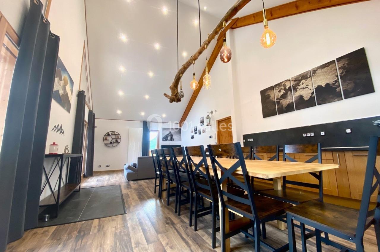 Salle à manger spacieuse avec table en bois, chaises noires, éclairage suspendu et plafond haut.