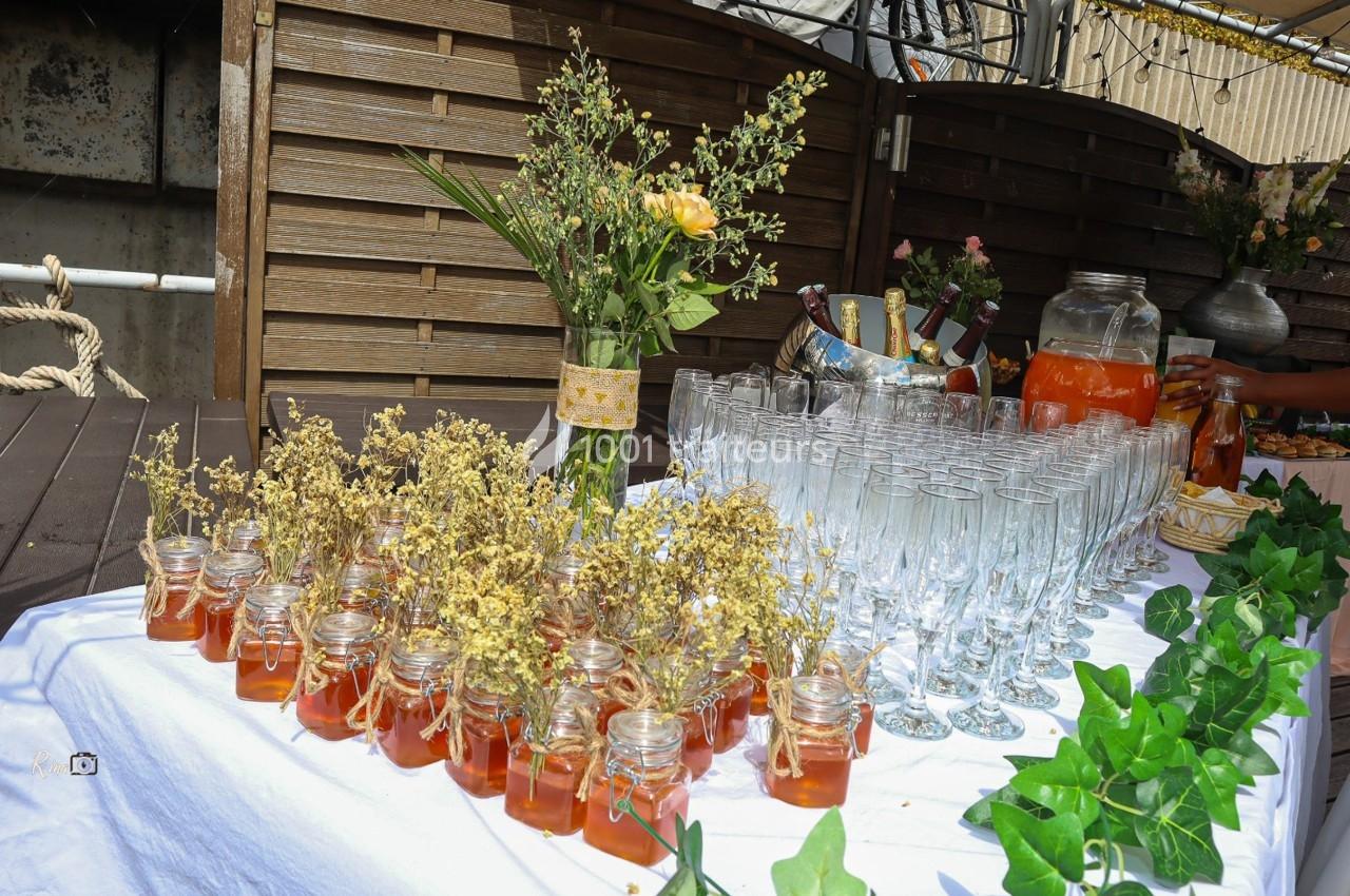 Table décorée avec des pots de miel, des fleurs séchées, des verres à pied et des boissons pour un événement en extérieur.