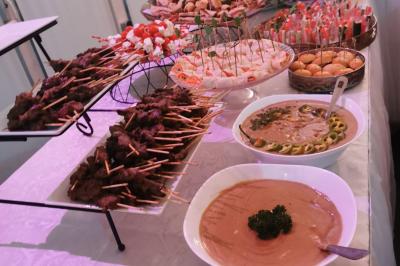Buffet avec brochettes de viande, verrines, pains garnis et sauces présentés sur une table blanche.