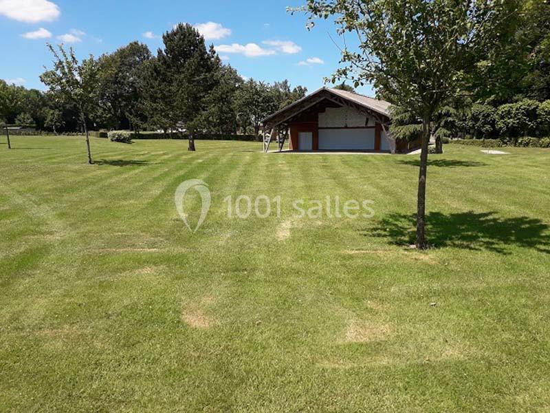 Pelouse bien entretenue avec un abri en bois au fond, entouré d'arbres et sous un ciel bleu dégagé.