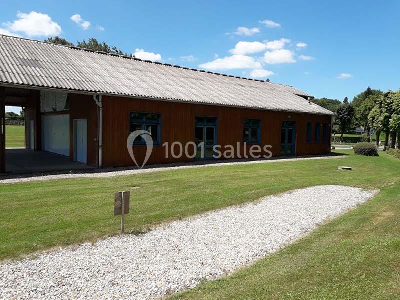 Bâtiment en bois avec toit en tuiles, entouré de pelouse et d'un chemin de gravier sous un ciel dégagé.