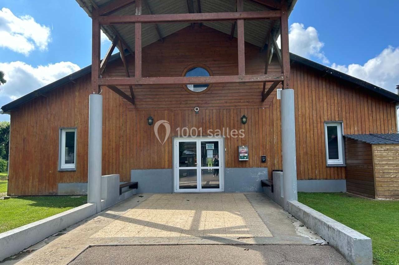 Façade d'un bâtiment en bois avec une entrée vitrée, entourée de pelouse et sous un ciel partiellement nuageux.