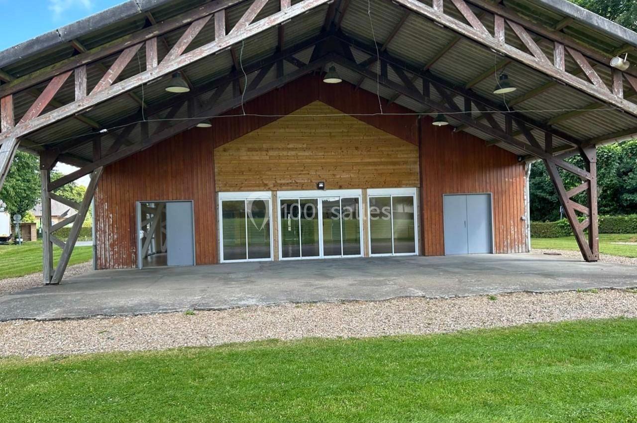 Structure en bois avec façade vitrée et portes grises, entourée de pelouse et d'arbres en arrière-plan.