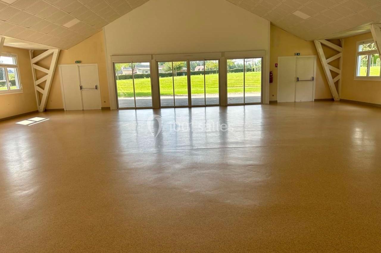 Salle vide avec sol en linoléum clair, grandes fenêtres laissant entrer la lumière naturelle et plafond incliné.
