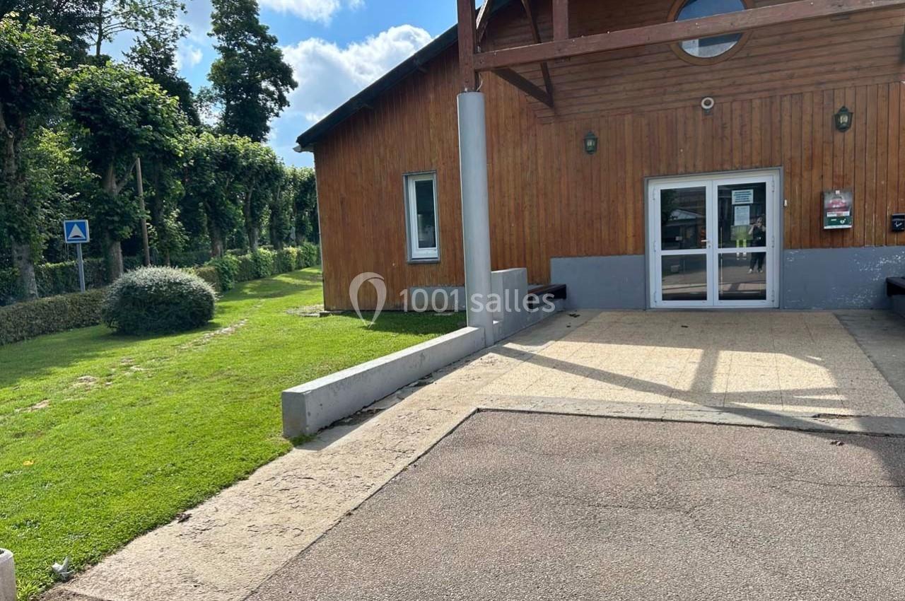 Entrée d'un bâtiment en bois avec une porte vitrée, entourée d'espaces verts et d'un chemin pavé.