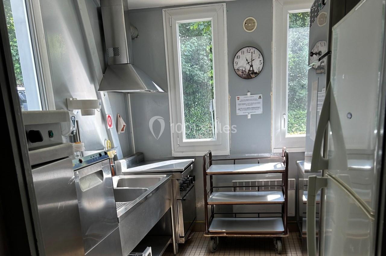 Cuisine professionnelle lumineuse avec équipements en inox, fenêtres donnant sur un extérieur verdoyant.