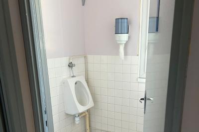 Toilettes avec lavabo, miroir, distributeur de papier, poubelle et carrelage au sol dans un espace restreint.