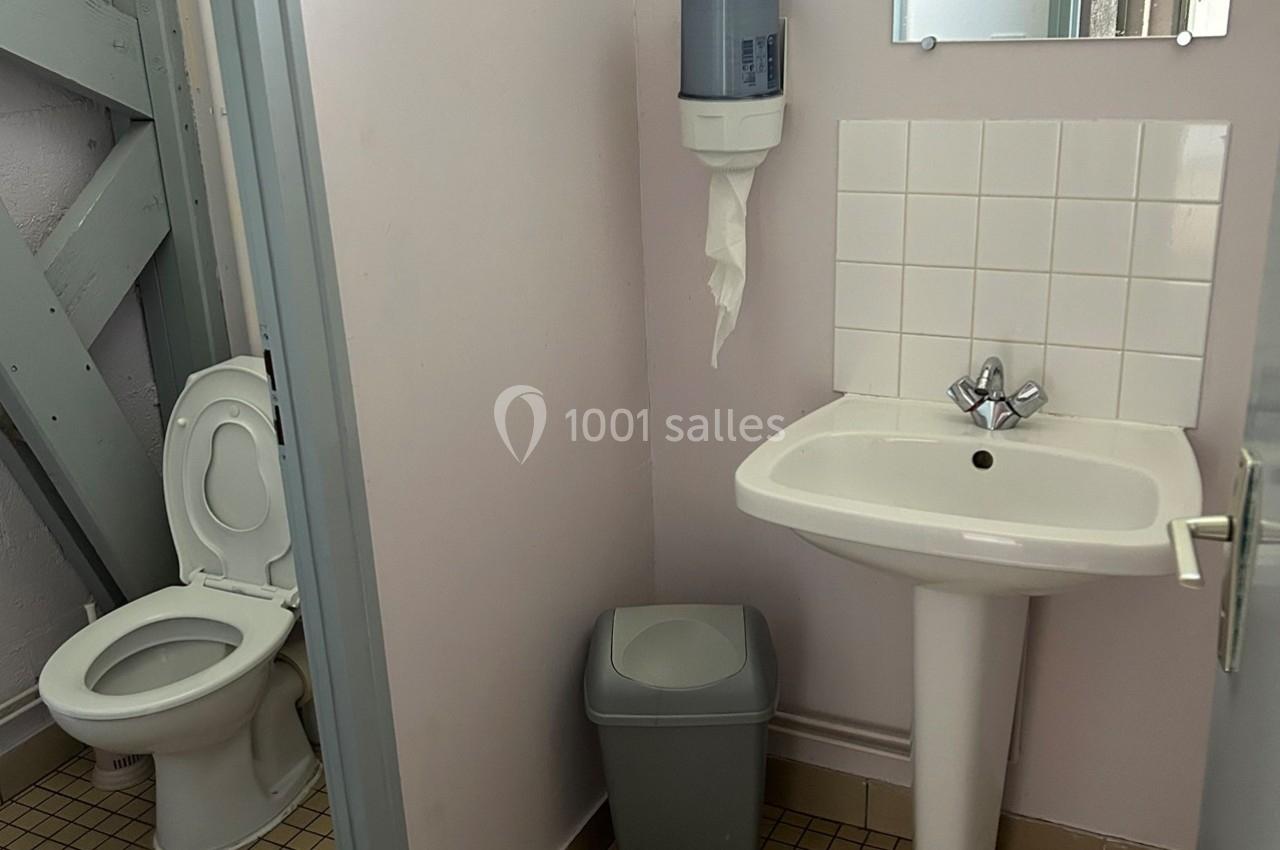 Toilettes avec lavabo, miroir, distributeur de papier, poubelle et carrelage au sol dans un espace restreint.